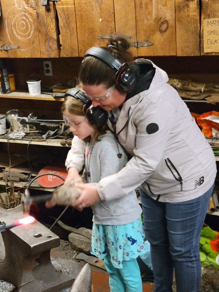 mom and child trying hammering on anvil
